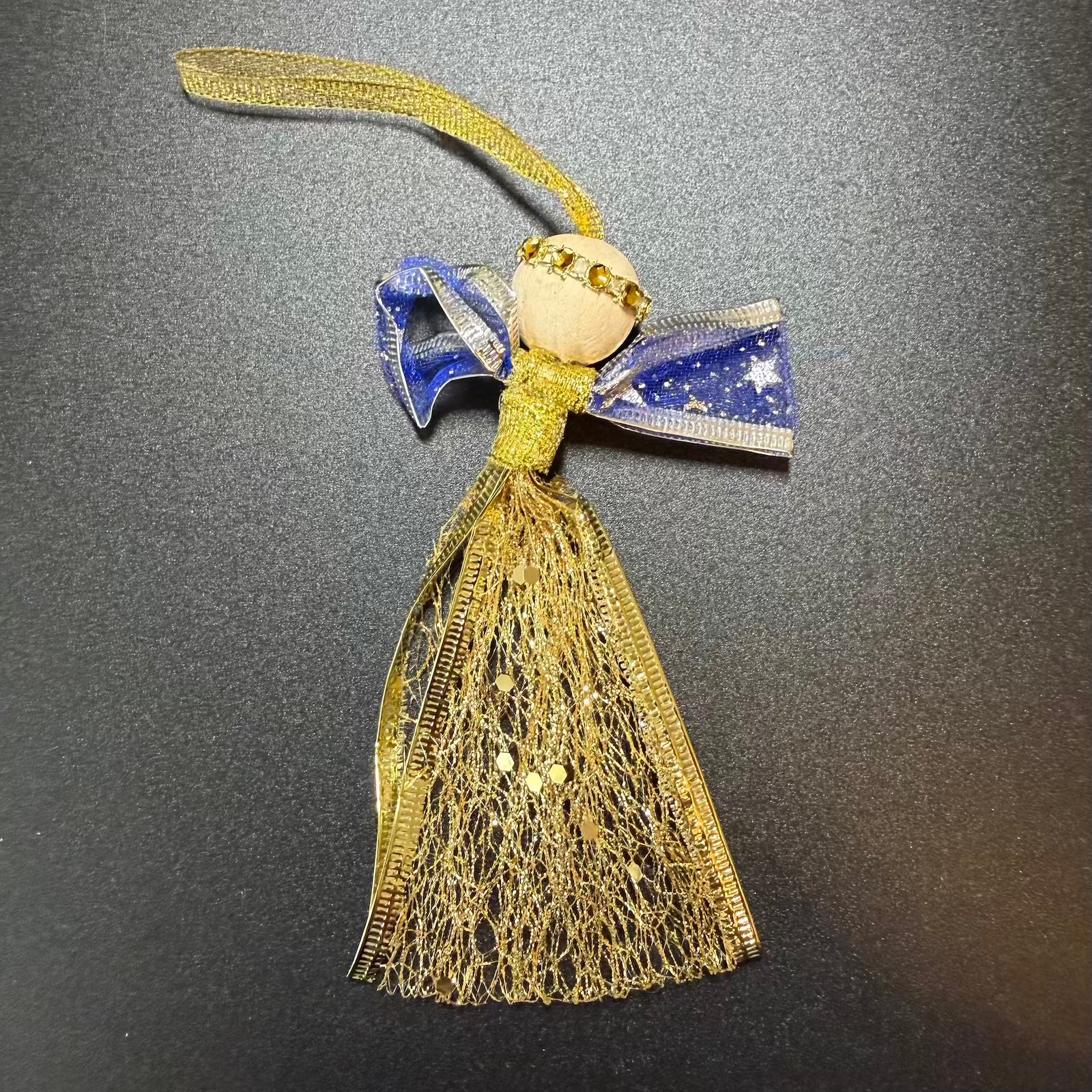 Decorative angel ornament with gold fabric and blue bow on a gray background