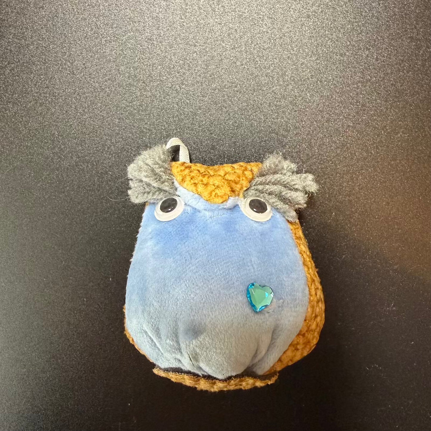 Small plush toy with blue body, yellow head, and gray hair on a dark background