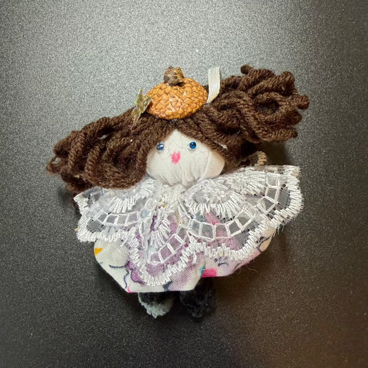 Small plush toy with brown hair and a white lace dress on a dark background