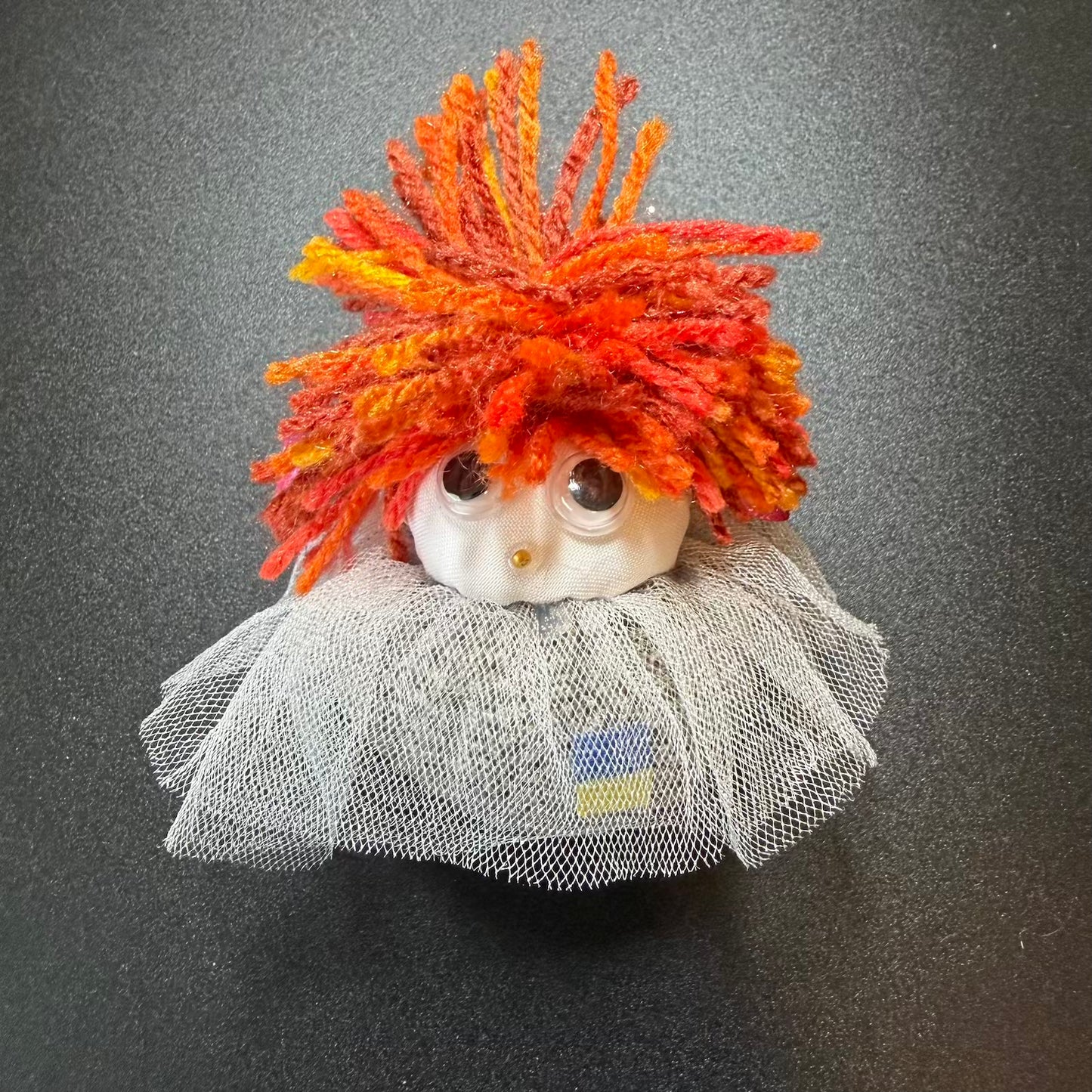 Small figurine with orange hair and a gray outfit on a dark background