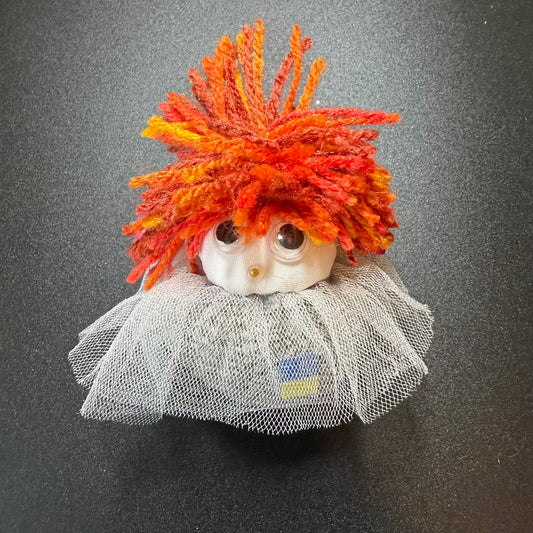 Small figurine with orange hair and a gray outfit on a dark background