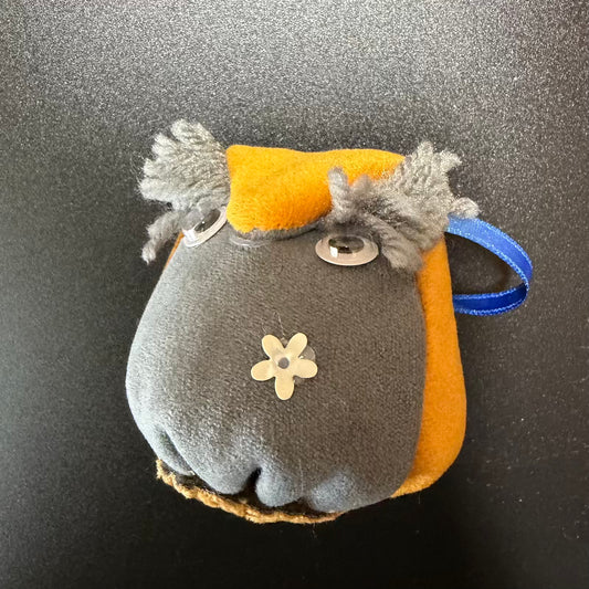 Plush keychain with gray face and orange body on a black background