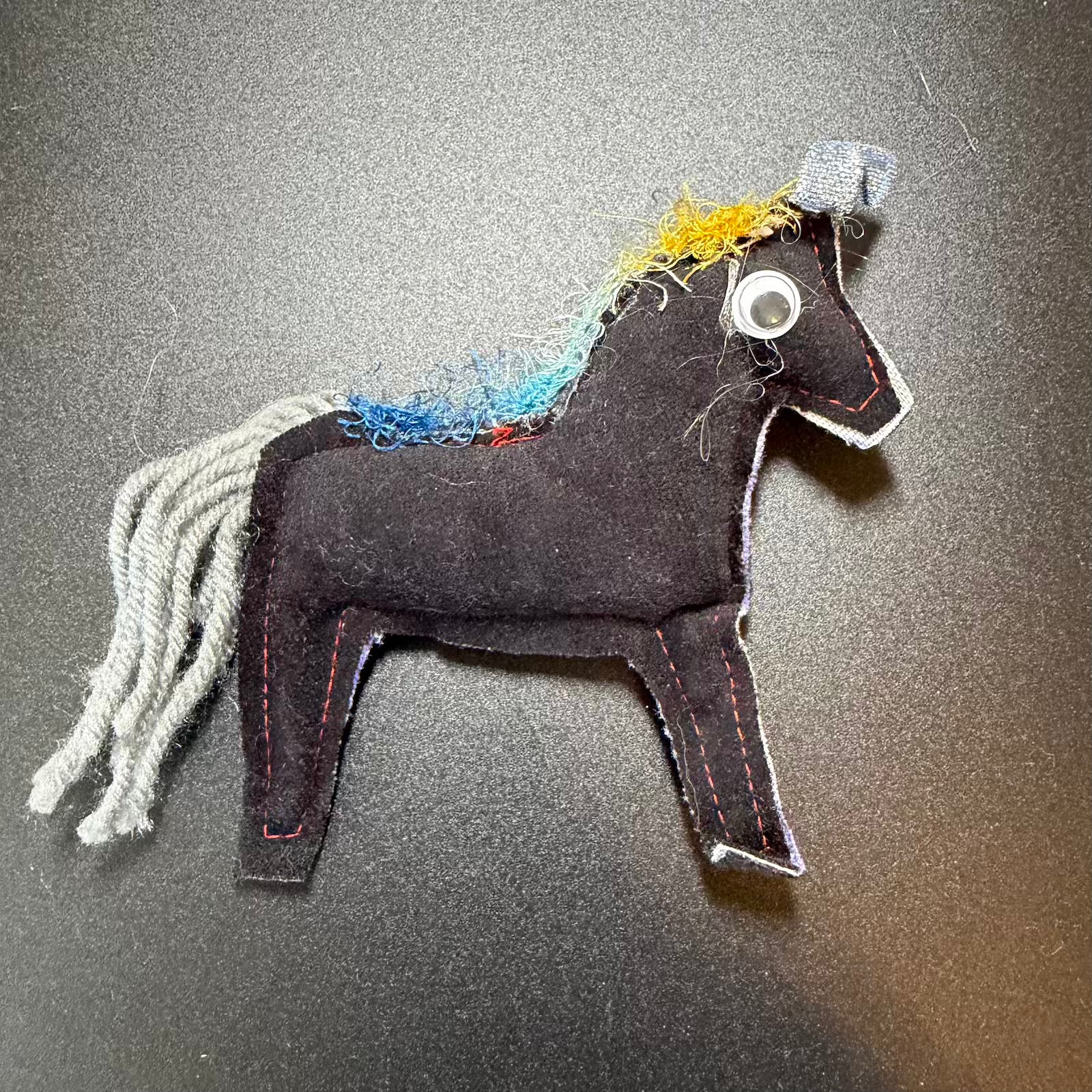 Handmade horse toy with colorful mane on a gray background