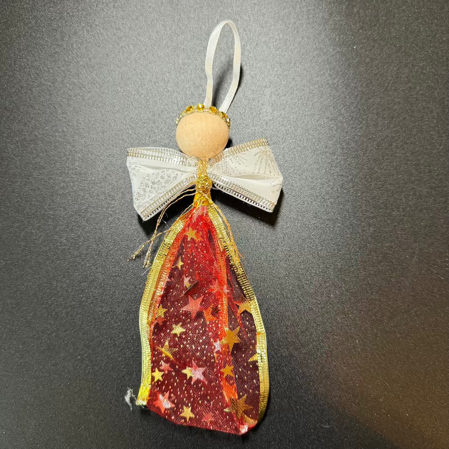 Decorative angel ornament with red and gold star pattern on a dark background