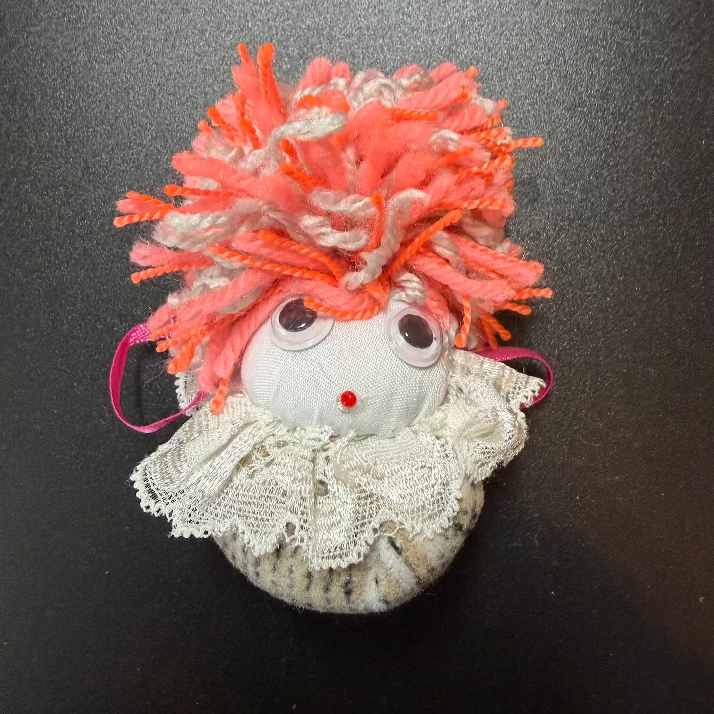 Small decorative figure with orange hair and lace details on a black background