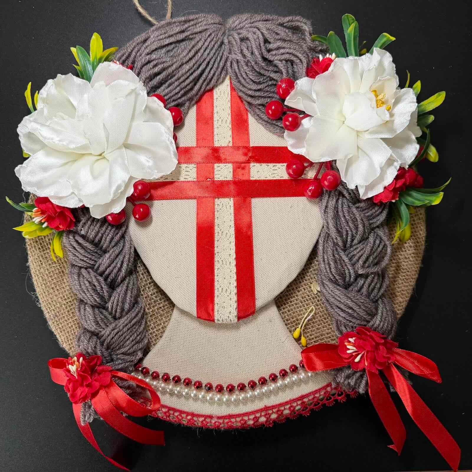 Decorative wreath with flowers, ribbons, and a red cross on a black background