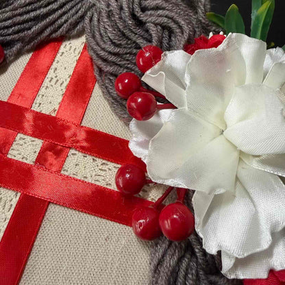 Close-up of a decorative item with red berries, white flower, and red ribbon on a textured surface.