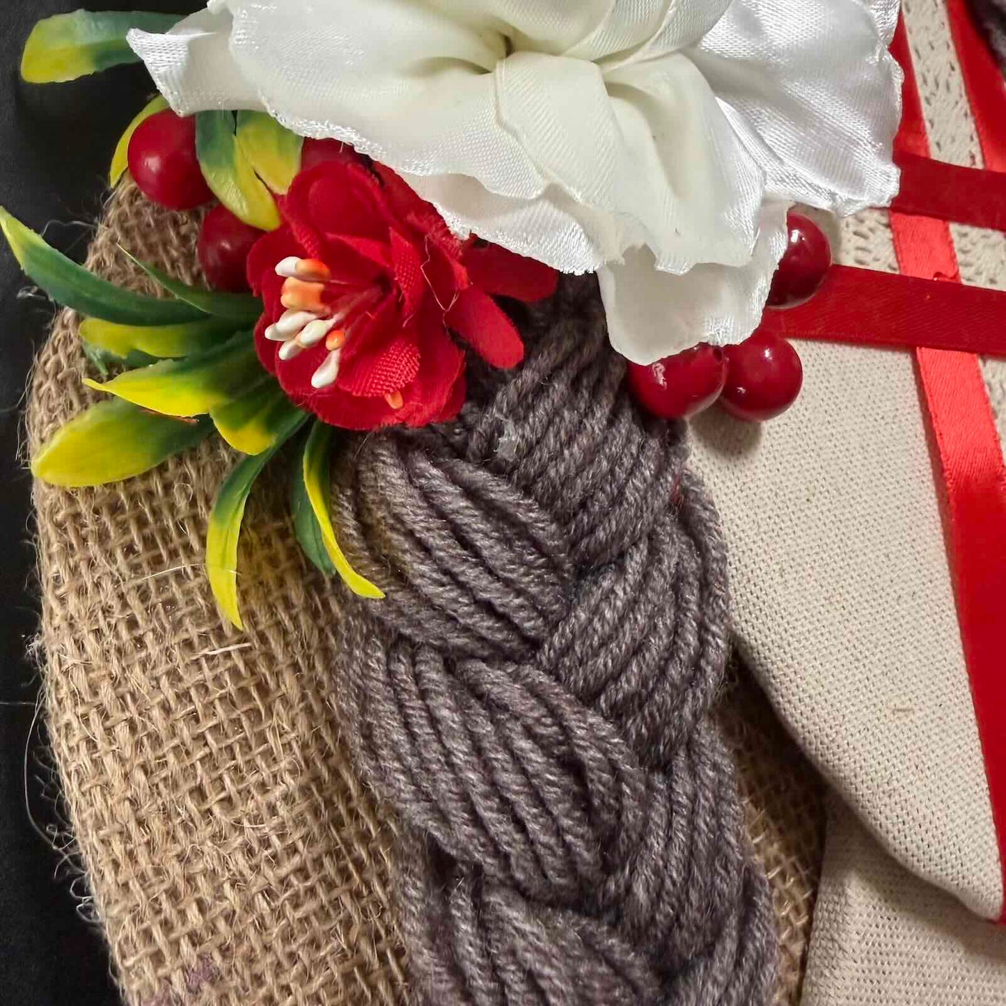 Decorative item with braided yarn, flowers, and red berries on a textured surface.