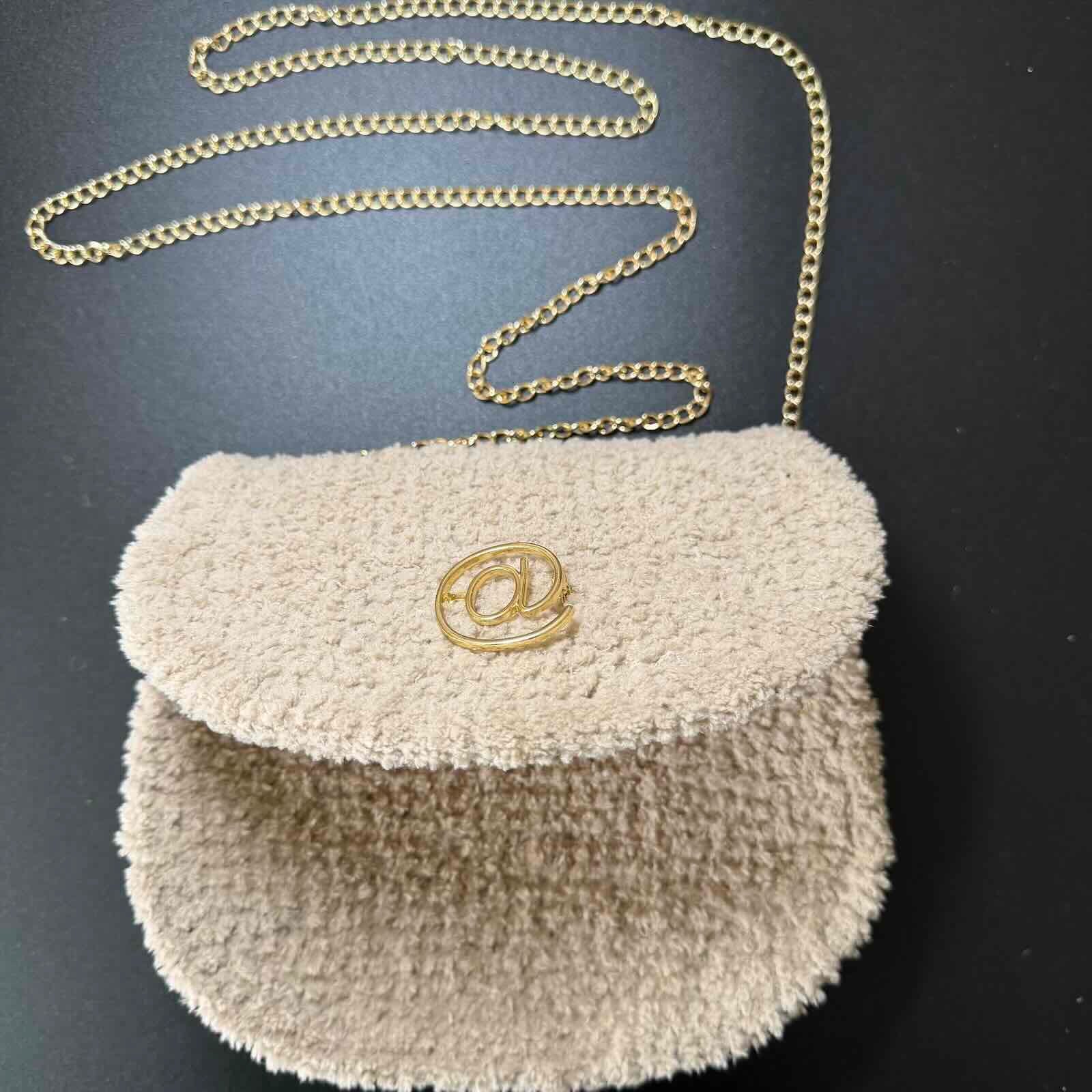 Beige textured handbag with gold chain strap on a dark background