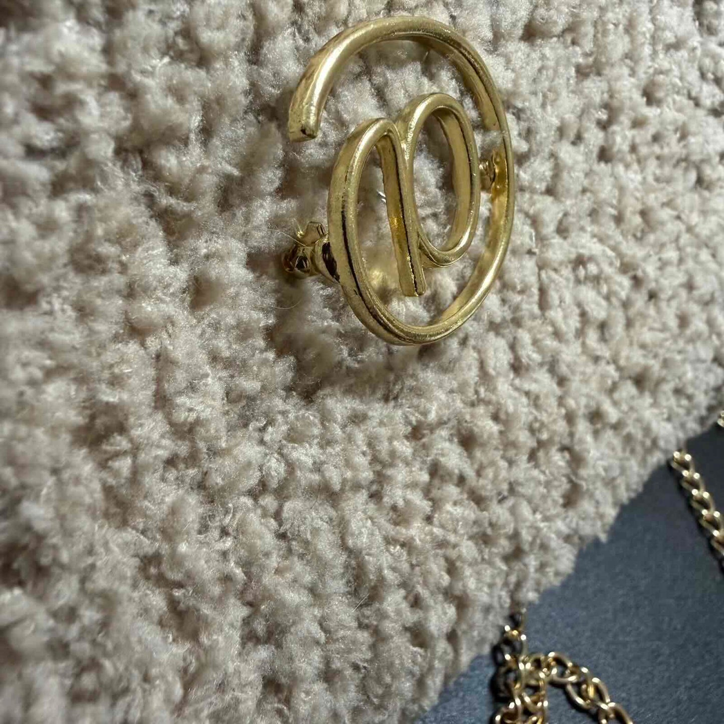 Gold earring with 'W' design on a textured surface