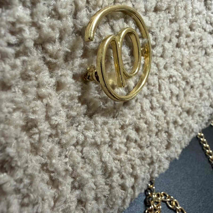 Gold earring with 'W' design on a textured surface