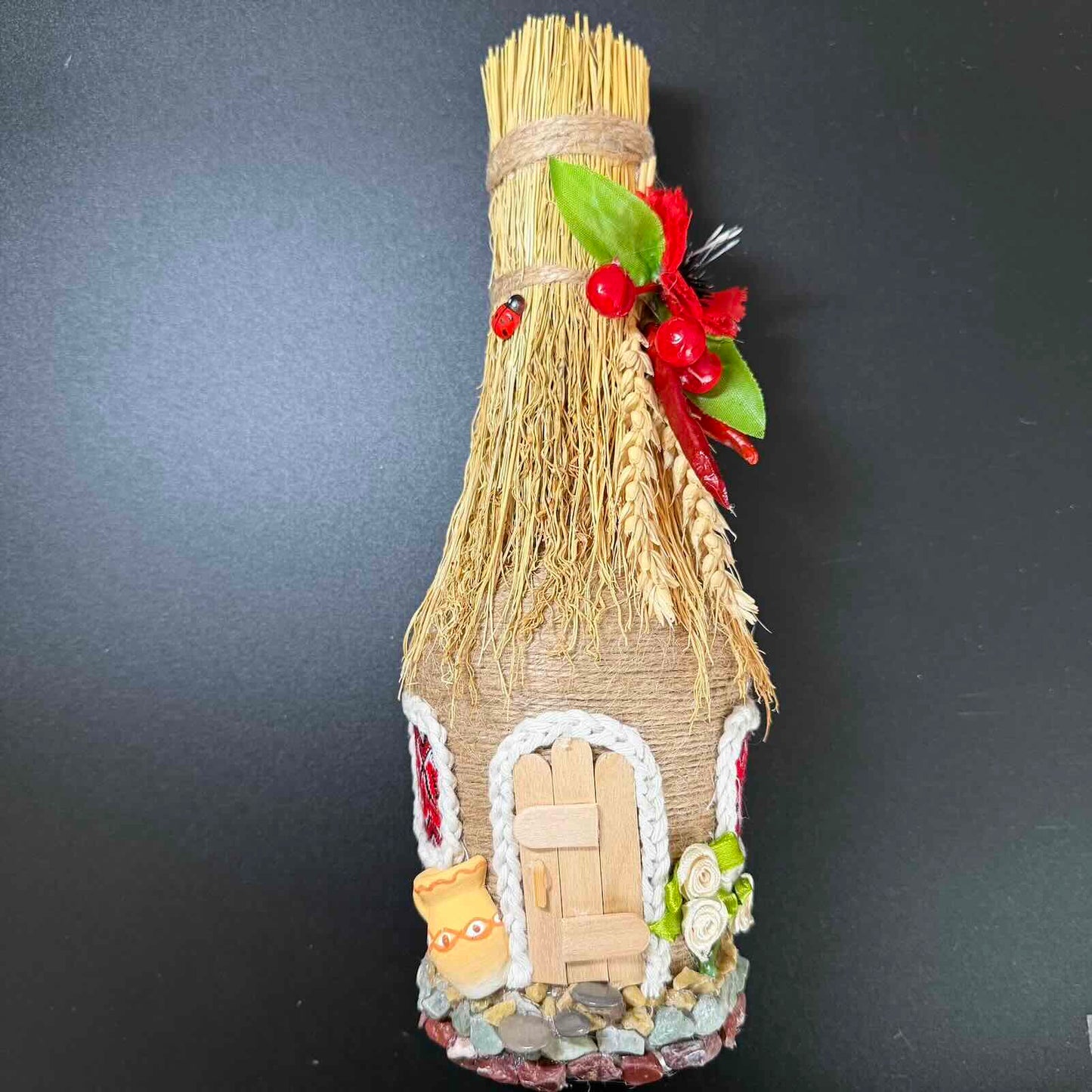 Decorative bottle house made from straw with a small door and windows on a black background