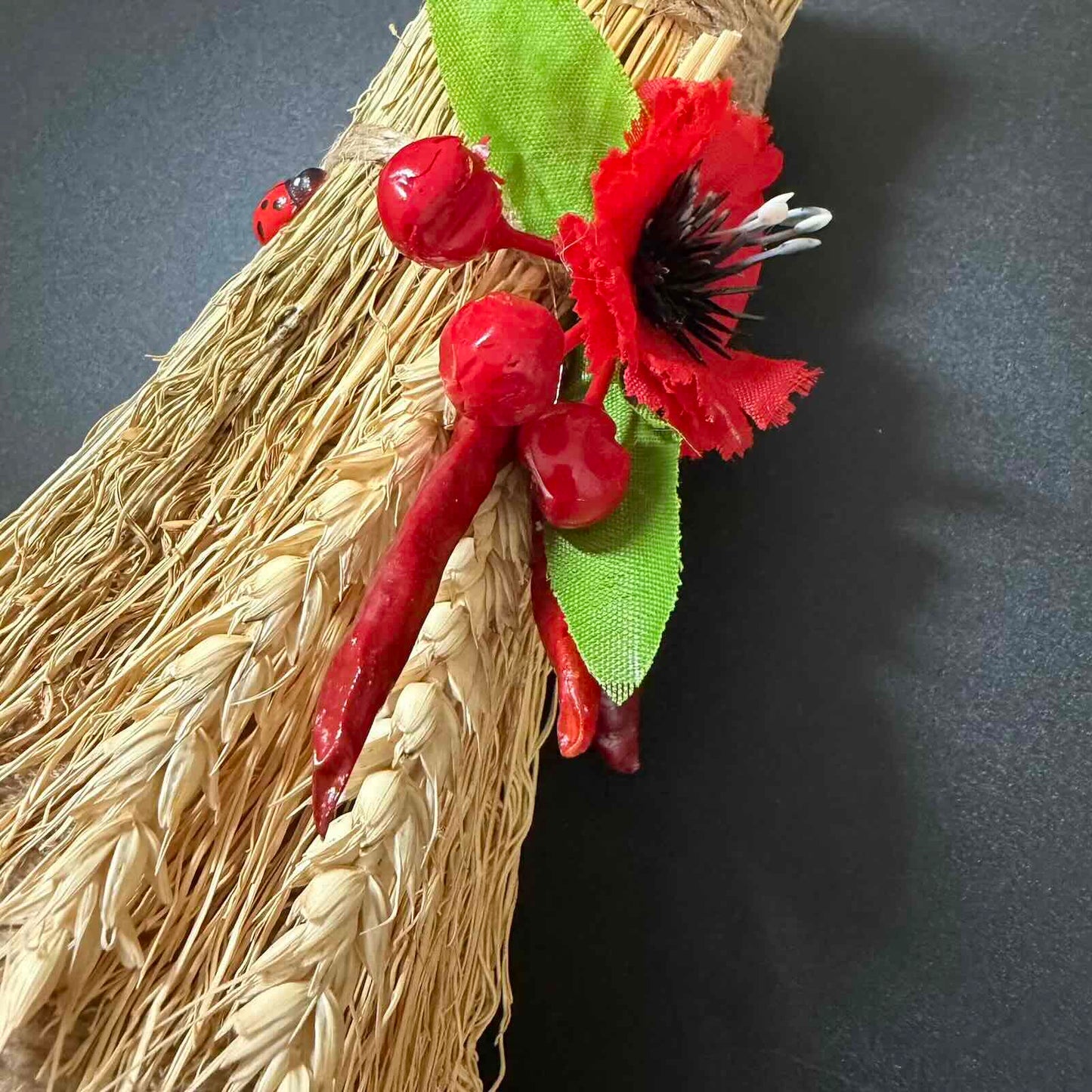 Decorative broom with red flowers and leaves on a dark background