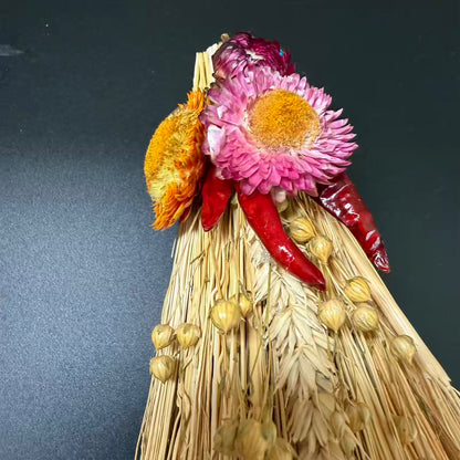 Decorative broom with dried flowers and red peppers against a dark background