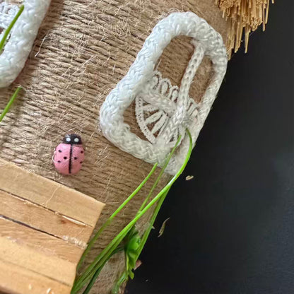 White crocheted item on a textured surface with a pink ladybug and green leaves.
