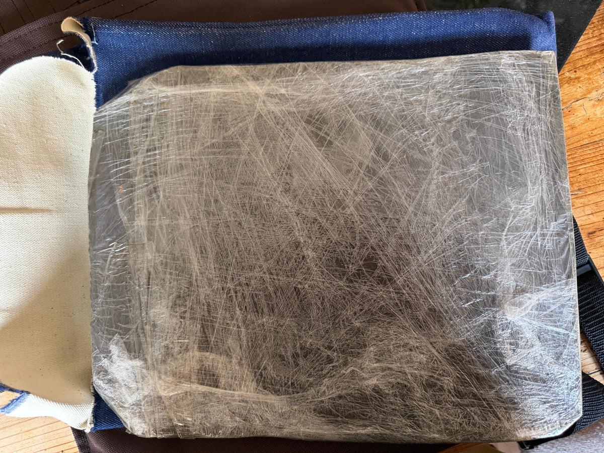 Close-up of one handmade steel armour plate covered with fibrous anti-spall material and tightly wrapped in clear plastic film.