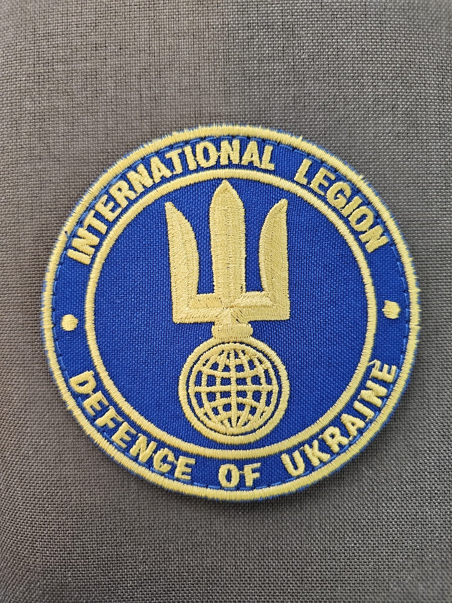 Circular fabric patch in blue and yellow with International Legion written on the edge with Ukraine Trident over a globe in the middle.