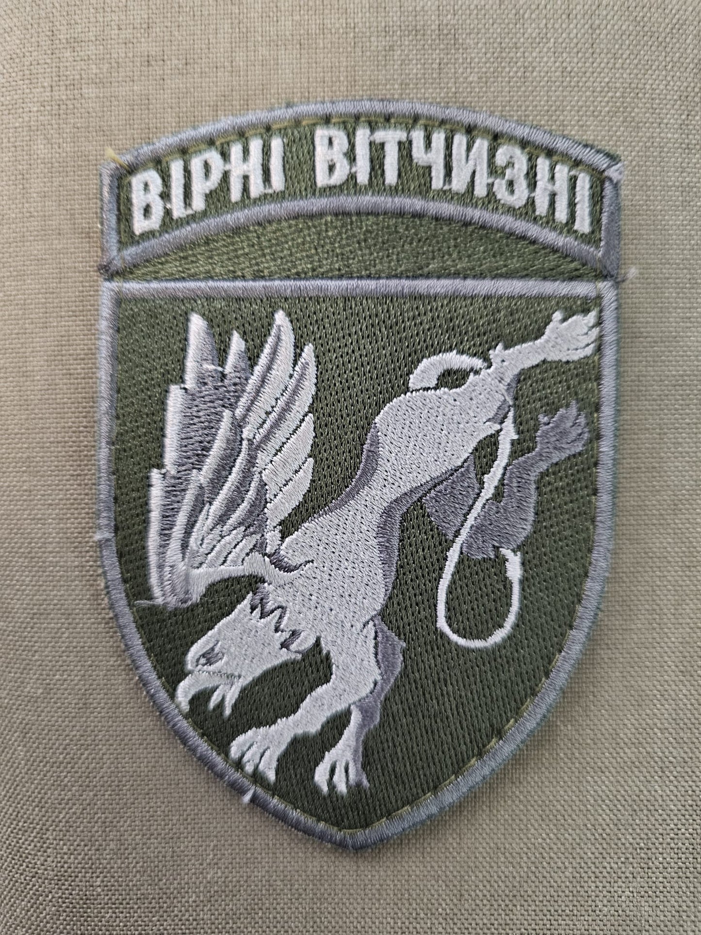 Silver Green fabric patch depicting a Griffen diving as it to grab the enemy, The text reads Faithful to the Homeland