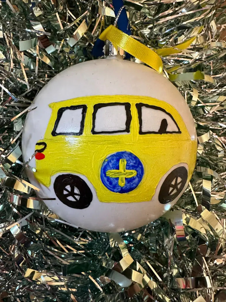 A hand-painted Christmas bauble featuring a yellow and black vehicle with a blue and yellow checkered pattern, set against a glittery background.