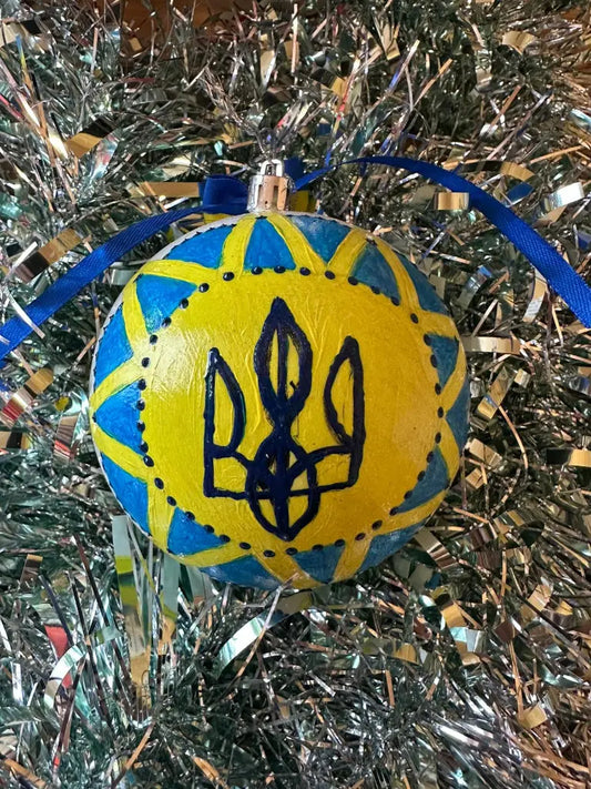 Hand painted Christmas bauble with a yellow and blue design, featuring a geometric emblem, displayed on a Christmas tree with blue and silver ornaments.
