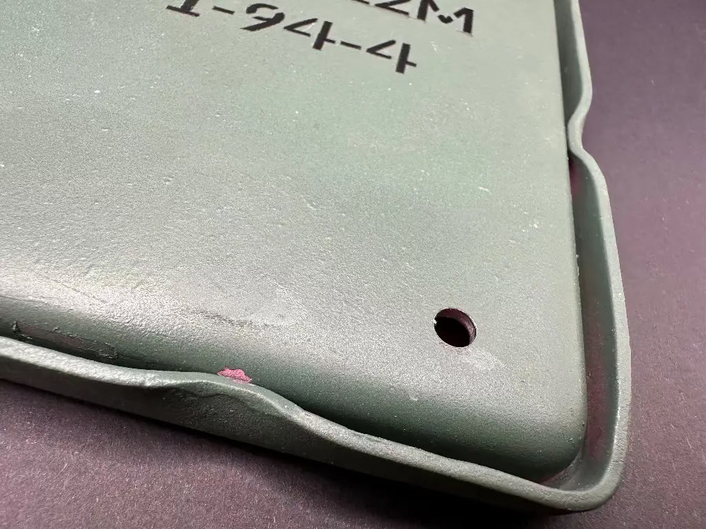 Close-up of a green plastic component with text and a hole on a gray background