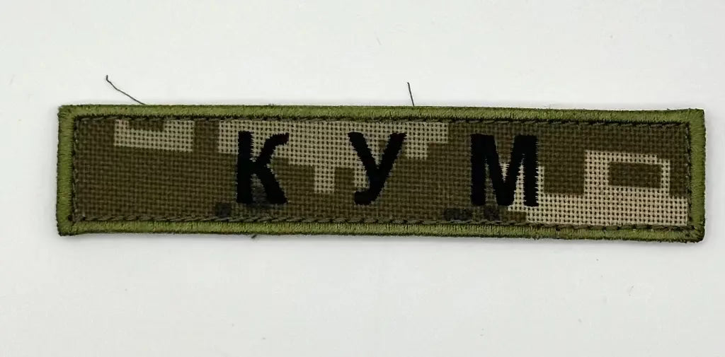 Textile patch with 'KUM' on a green background