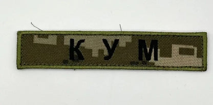 Textile patch with 'KUM' on a green background