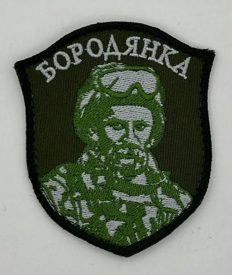 A green and black patch featuring a pixelated camouflaged image with the text 'БОРОДЯНКА' on it.