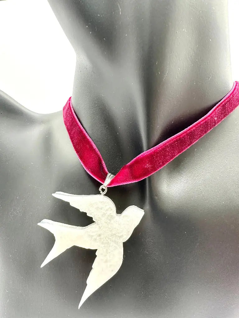 Necklace with a bird pendant on a mannequin wearing a red velvet ribbon.